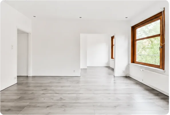Lege kamer met lichte houten vloer, twee ramen en open deuropening voor renovatie.